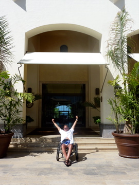 Chris cheering with both arms raised outside a hotel entrance