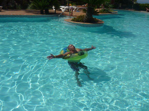 Chris floating with arms outstretched in a bright blue pool