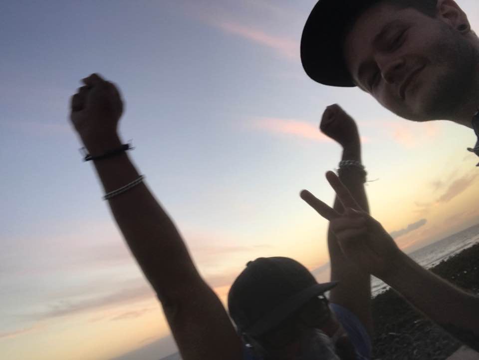 Celebrating beside the sea at sunset with my carer and good friend—arms raised and enjoying the moment together.