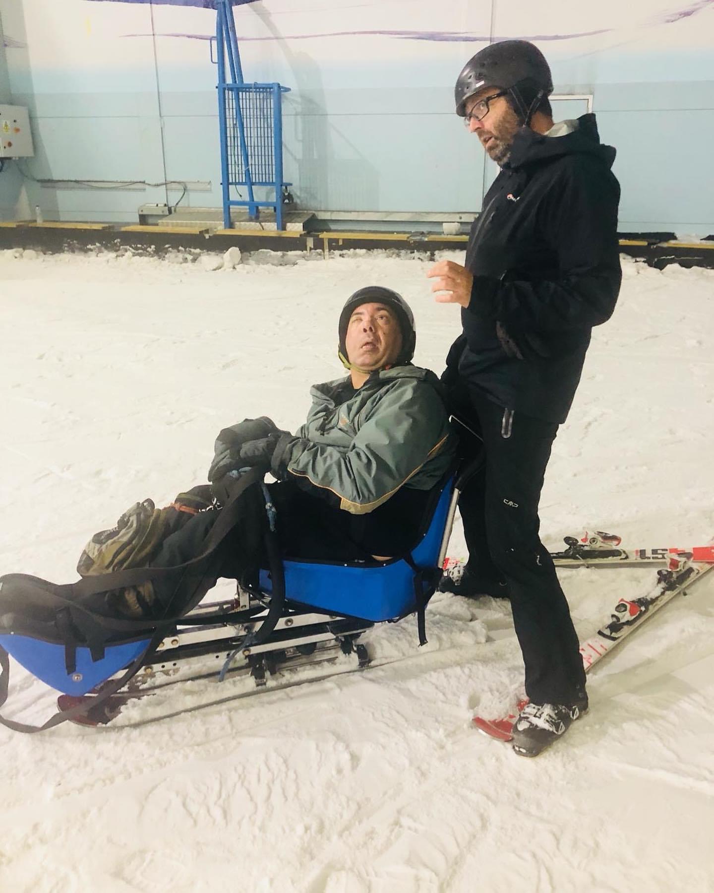 Chris in a sit-ski on the snow with his instructor beside him